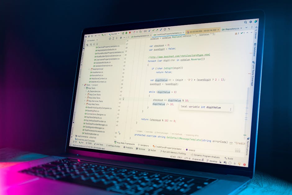 A close-up view of a laptop screen displaying lines of code in a programming editor, with a dark keyboard illuminated by soft pink and blue lighting. The screen shows a variety of code snippets, inclu